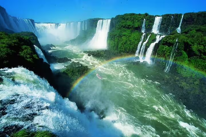 Stunning rainbow arches over Iguazu Falls viewed from Argentina, highlighting the lush greenery and cascading water.