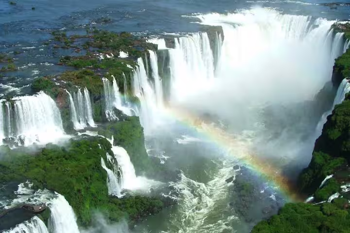 Breathtaking view of Iguazu Falls with vibrant rainbow arching through misty cascades and lush green landscape.