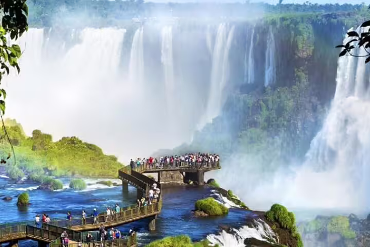 Visitors on a viewing platform enjoy the majestic Iguazu Falls, capturing the vibrant mist and verdant landscape.