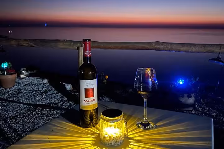 Candlelit bottle of Lagriros red wine and glass on a seaside terrace at sunset during Ikaria family-run winery tour