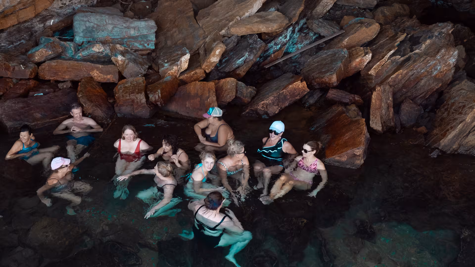 Happy travelers relaxing together in Ikaria’s rocky seaside hot springs, enjoying the island’s famous natural thermal waters