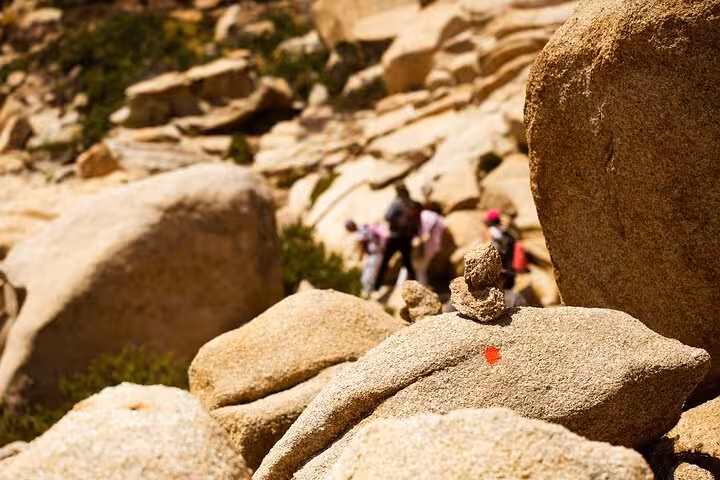 Marked rocky trail with hikers in the background on Ikaria’s west side, showcasing adventurous coastal walking routes.