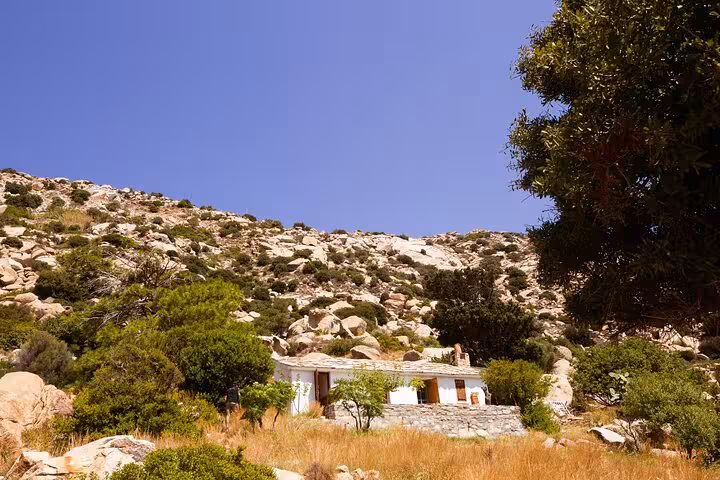 Traditional stone house nestled among rocky hills and green shrubs on the sunlit west side of Ikaria