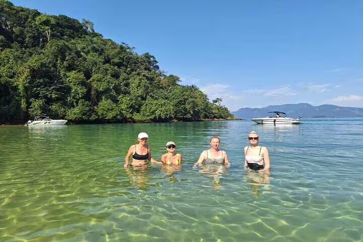 Visitors swimming in clear waters of Ilha Grande with lush green backdrop, part of Angra boat tour experience.