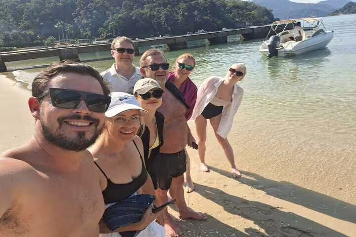 Group enjoying a sunny day on Ilha Grande beach, with a private boat ready for a tour, barbecue, and drinks adventure.