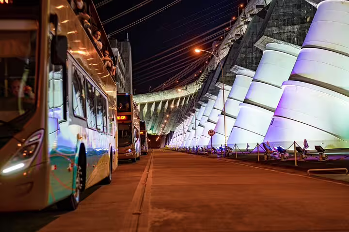 Night view of illuminated Itaipu Dam with tour buses, highlighting a unique aspect of the Iguazu Falls tour.