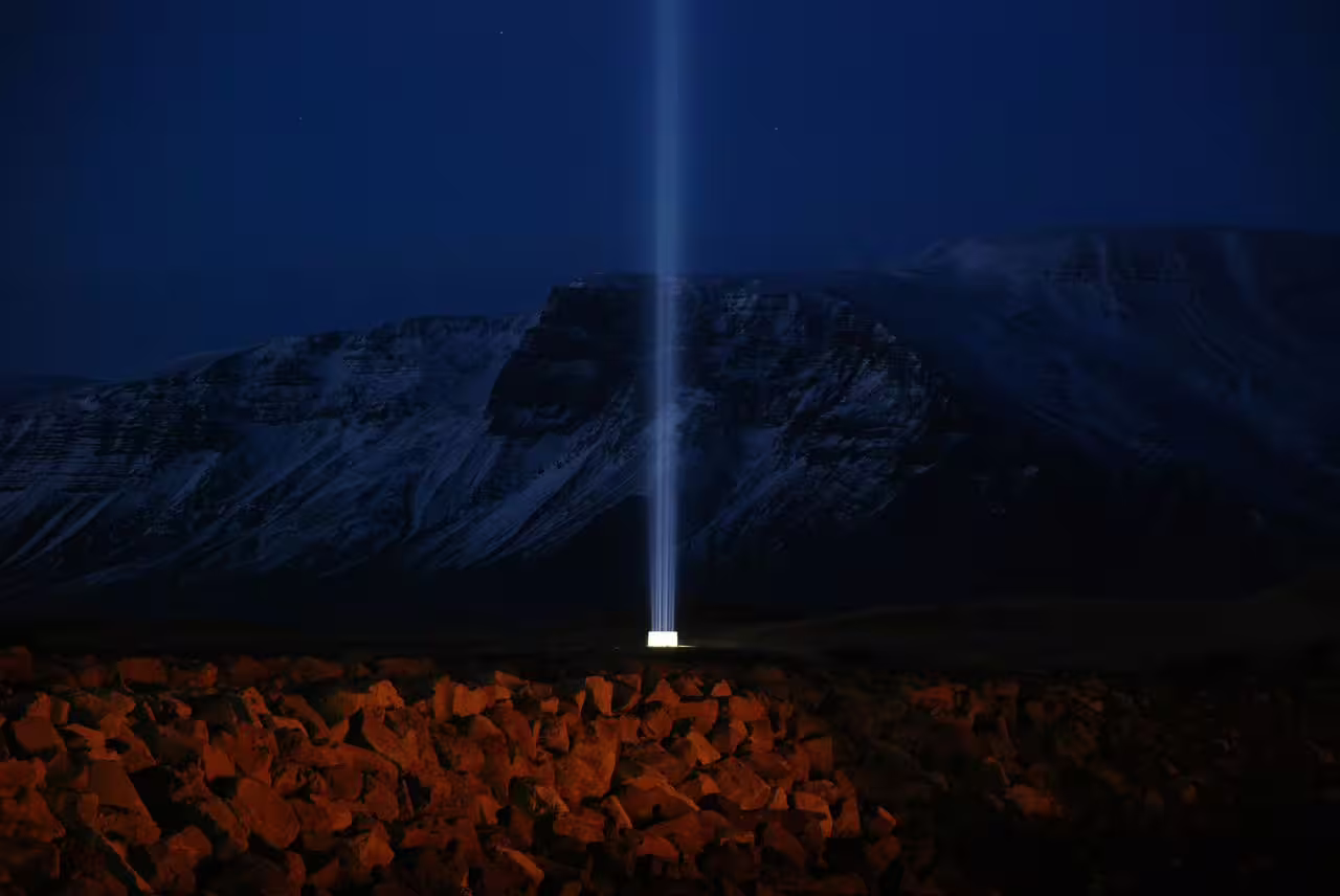 Imagine Peace Tower beam of light shining into night sky with snow-capped mountains on Videy Island Iceland