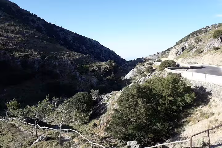 Scenic view of Imbros Gorge from a winding road, showcasing lush greenery and rugged hills under a clear blue sky.