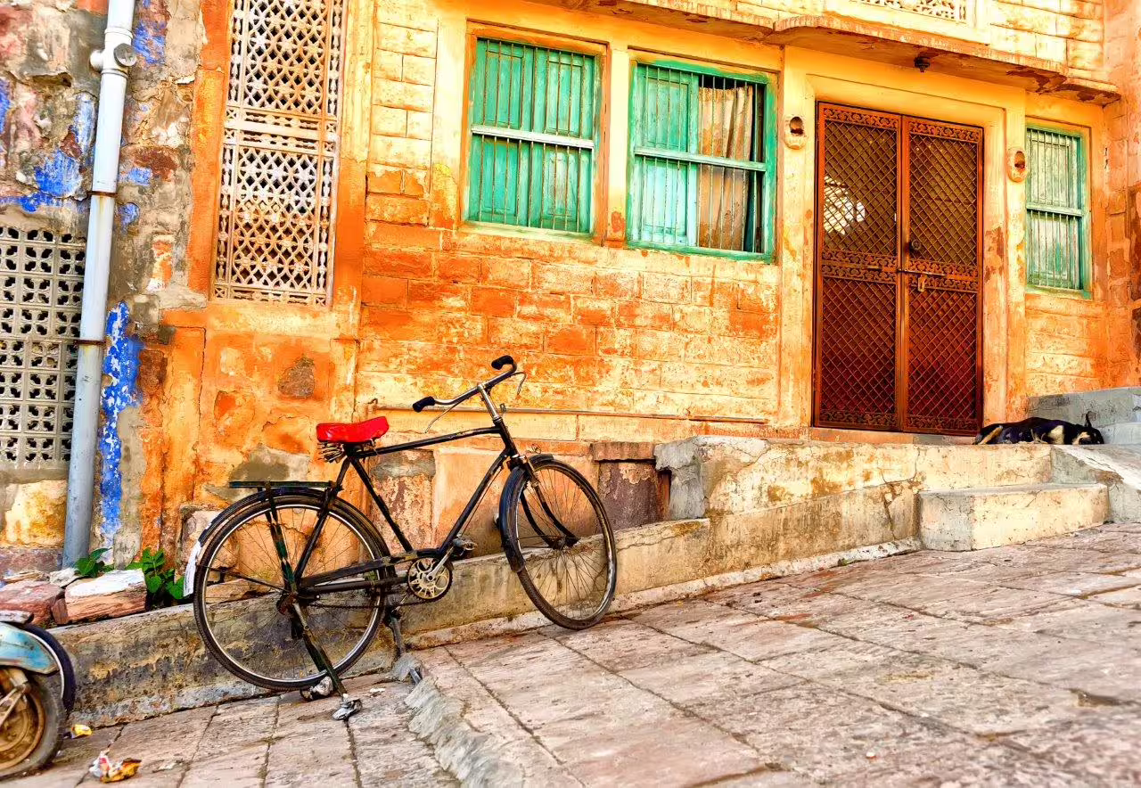 Charming rustic scene with a vintage bicycle leaning against a sunlit, ochre-colored wall in an Indian street setting.