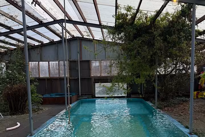 Indoor pool with turquoise water inside a greenhouse structure with plants and metal building