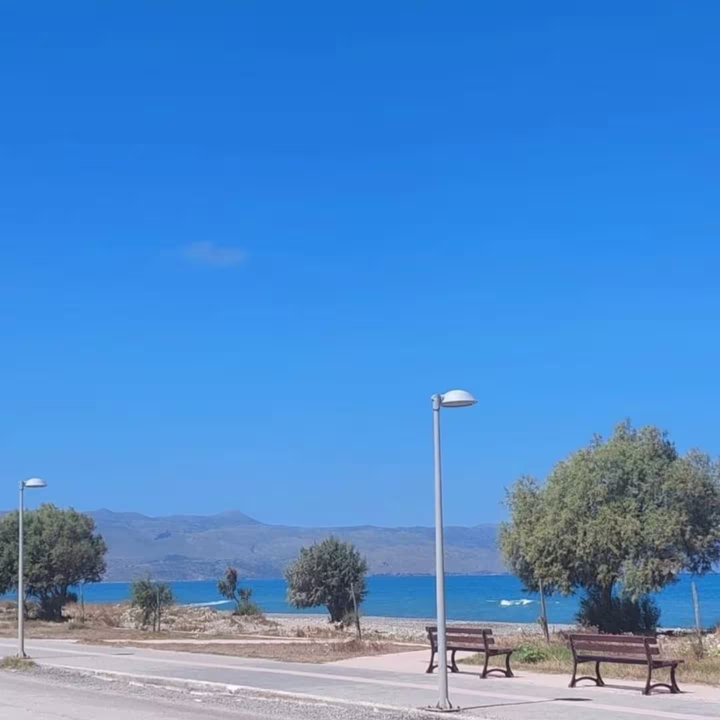 Scenic coastal view near Infinity Night Villa featuring a clear blue sky, tranquil sea, and inviting promenade benches.