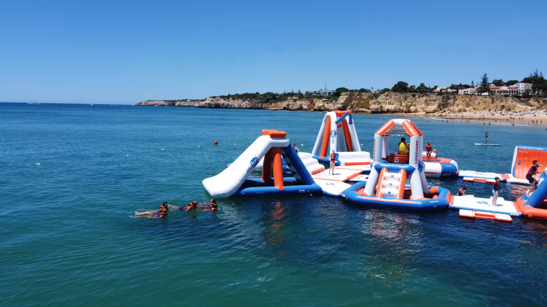 Aerial view of inflatable waterpark with slides and climbing frames anchored in turquoise ocean near Algarve beach