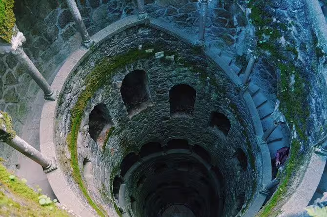 Moss-covered Initiation Well at Quinta da Regaleira, showcasing intricate stone architecture and spiral staircase.
