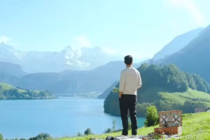 Man enjoys breathtaking views of Interlaken's lake and mountains, reminiscent of Crash Landing on You scenes.