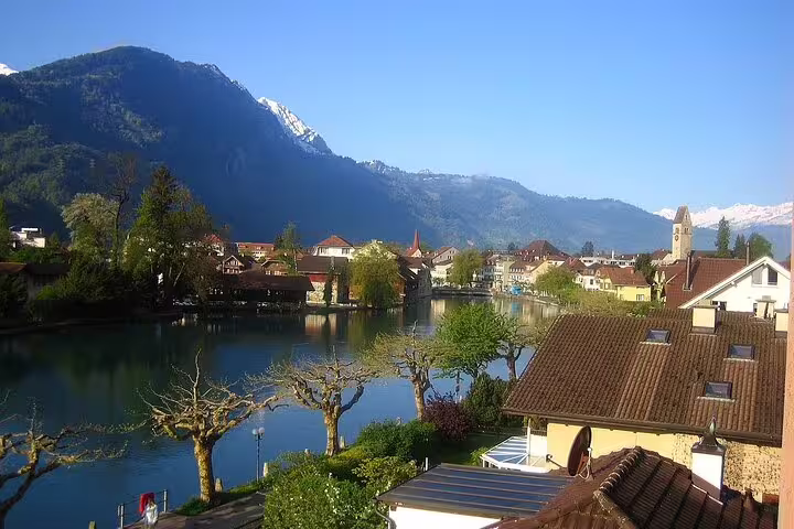 Interlaken town with river, alpine buildings, church tower, and snow-capped mountains under clear blue sky