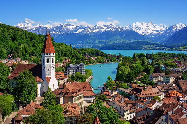 Aerial view of Thun old town with church tower, turquoise lake, and snow-capped Swiss Alps in background