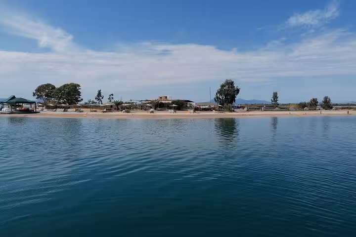 Calm Ionian Sea shoreline stop on local BBQ boat trip, sandy beach and blue water under clear skies