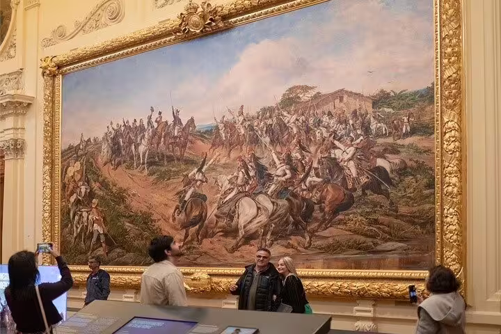 Visitors admire a historical battle painting at Ipiranga Museum, capturing pivotal moments in Brazil's past.