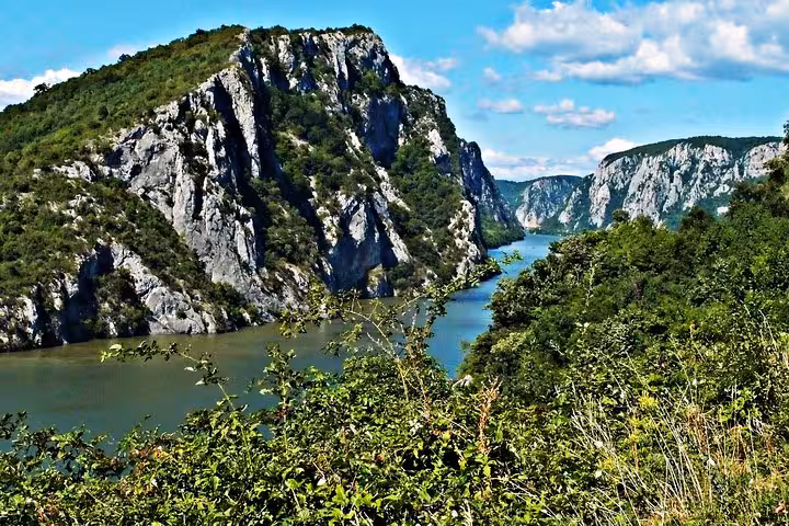 Scenic view of Iron Gate Gorge on the Danube River, surrounded by lush greenery and towering cliffs.