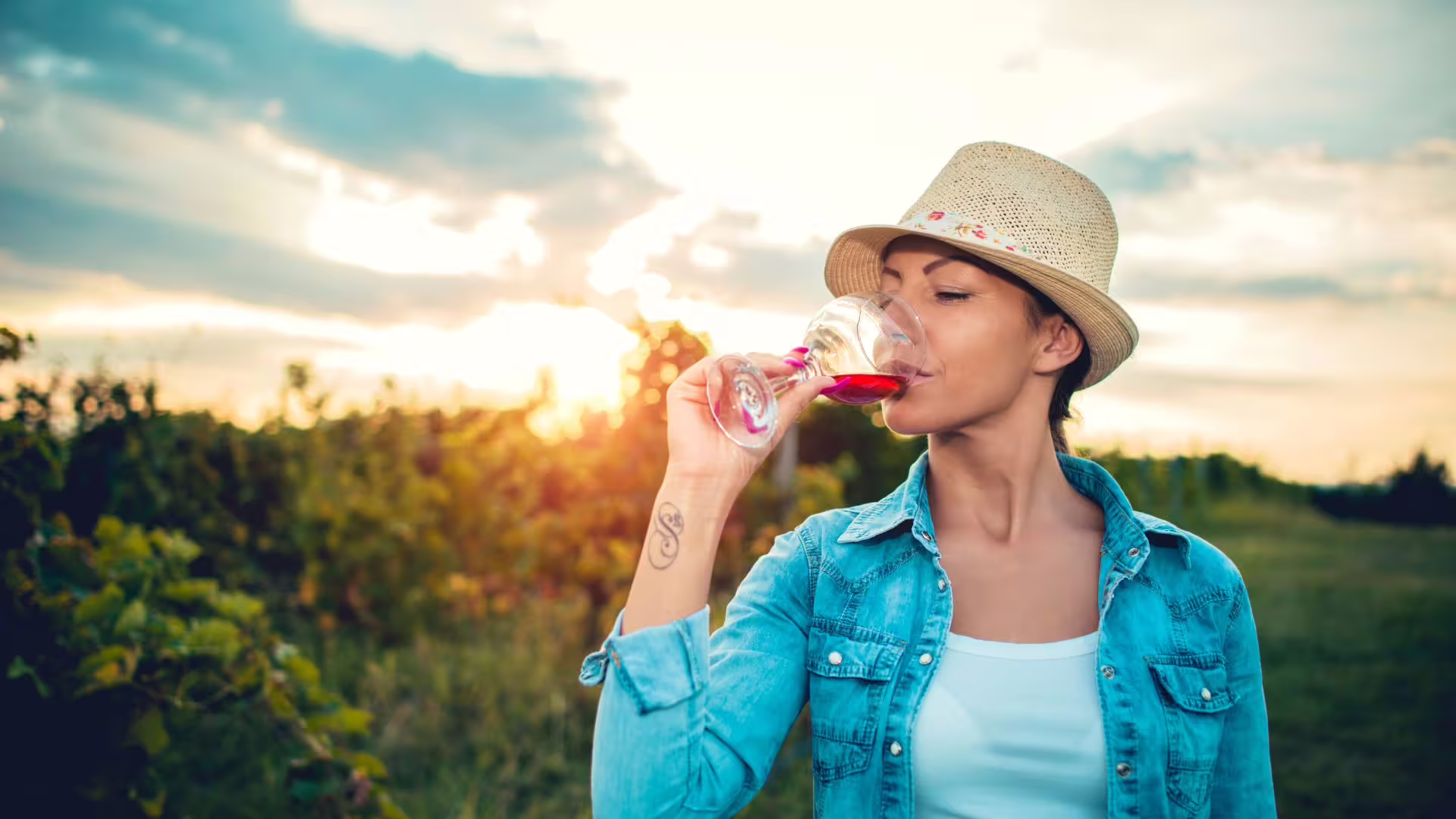 Woman in straw hat tasting red wine at sunset in an Irpinia vineyard, enjoying a guided wine tour experience