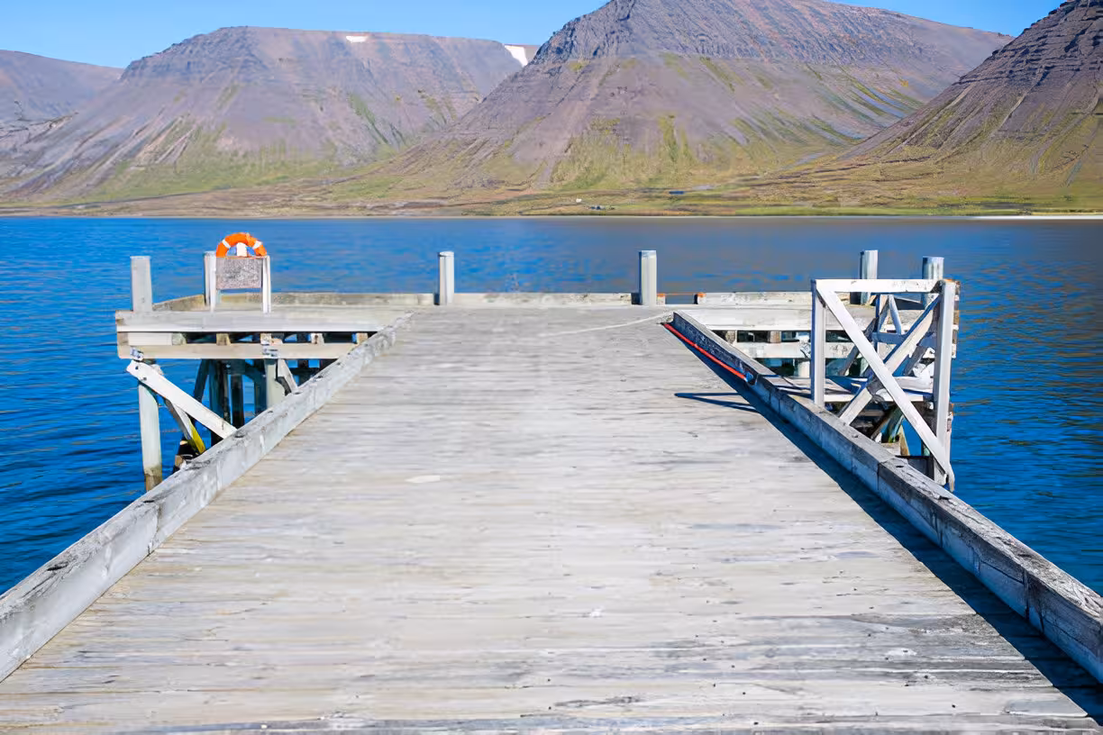 Wooden pier extending over blue fjord waters with dramatic mountains in Isafjordur, Westfjords Iceland
