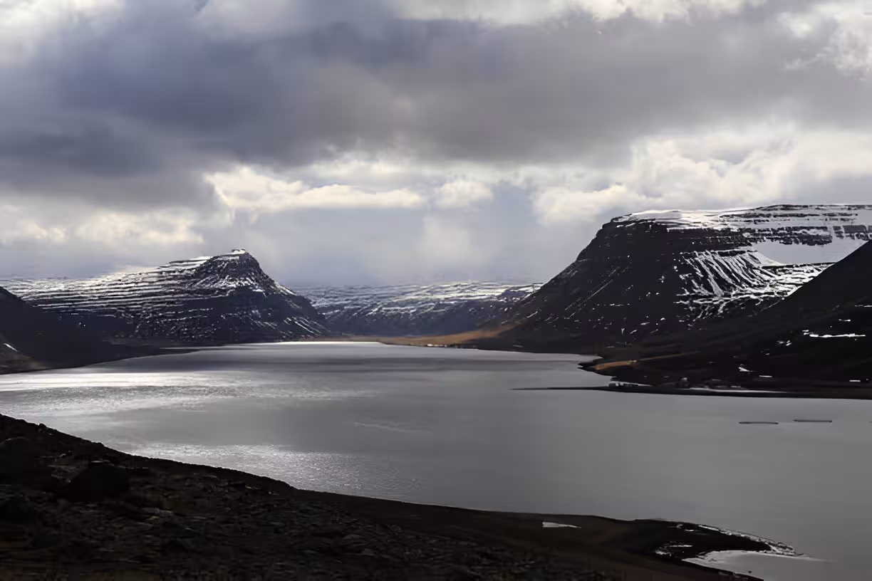 Snow-capped fjord mountains flanking calm waters near Isafjordur, Westfjords Iceland under dramatic cloudy sky