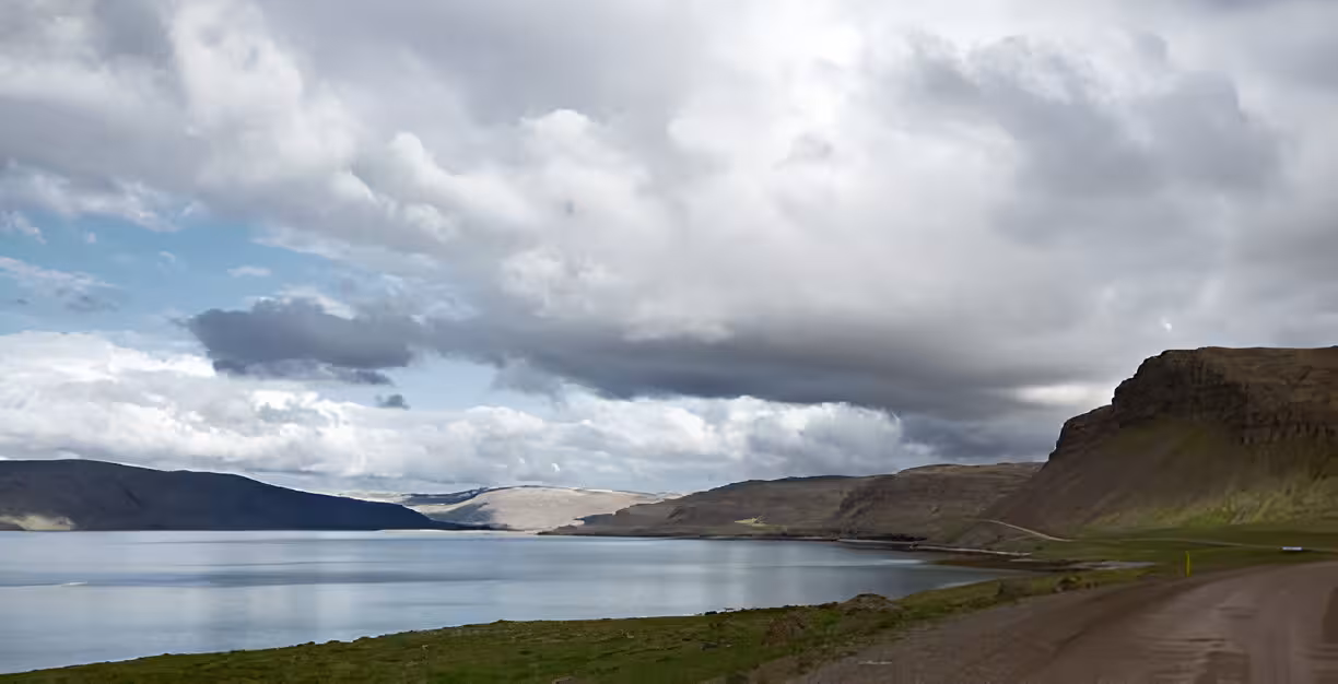 Calm fjord waters with dramatic clouds and steep cliffs along the road to Dynjandi Waterfall, Westfjords Iceland