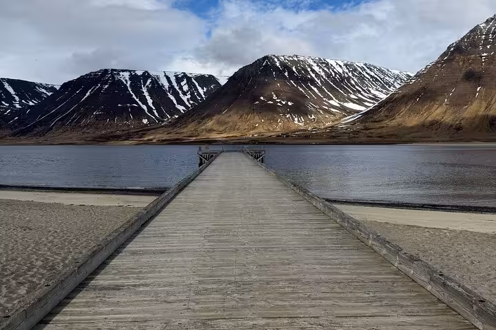 Wooden pier extending into calm fjord waters surrounded by snow-capped mountains in Isafjordur, Westfjords Iceland