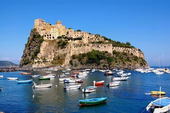 Discover Ischia's majestic Aragonese Castle surrounded by vibrant boats on the shimmering Tyrrhenian Sea.