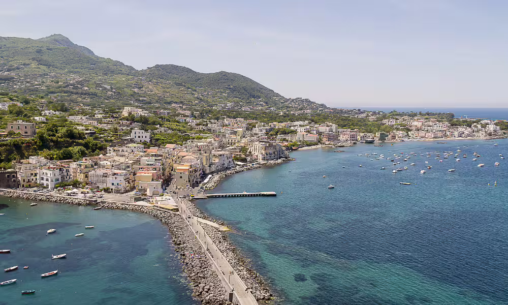 Aerial view of Ischia coastline with colorful houses, Mount Epomeo and boats, seen during a scenic Ischia boat tour