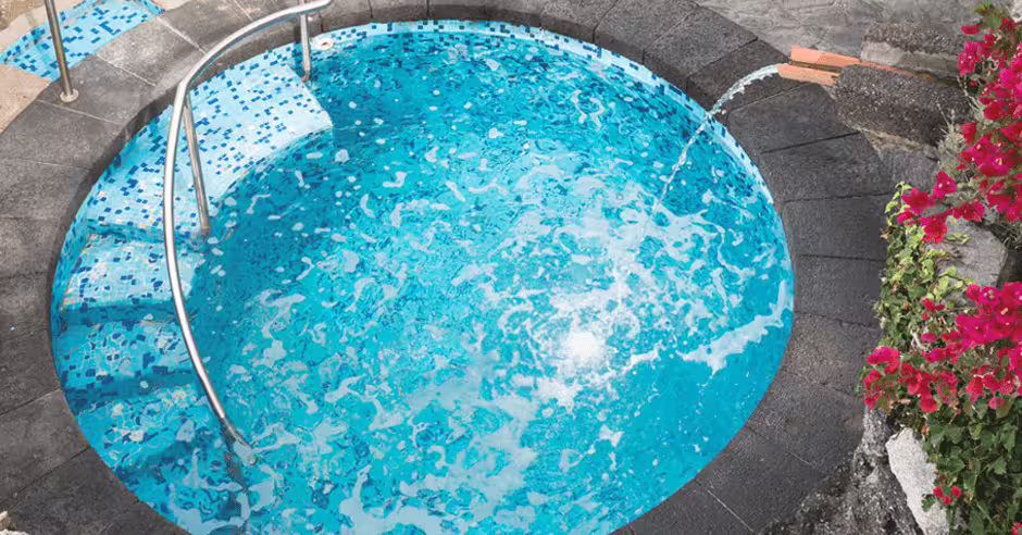 Piccola piscina termale circolare all’aperto al Parco Castiglione Ischia, con acqua azzurra, getto caldo e fiori colorati.