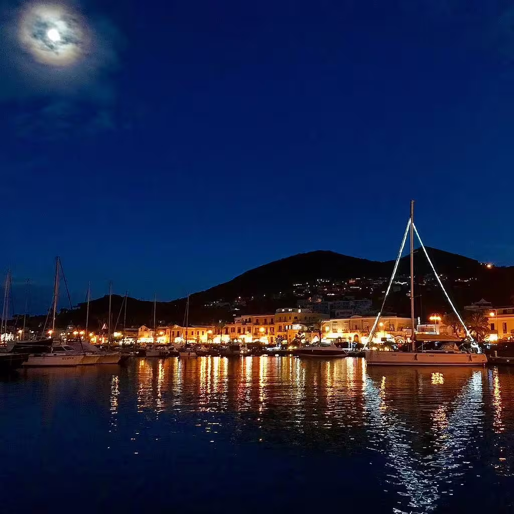 Lungomare di Ischia by night con barche ormeggiate, luci del porto riflesse sul mare e atmosfera della Festa di Sant’Anna