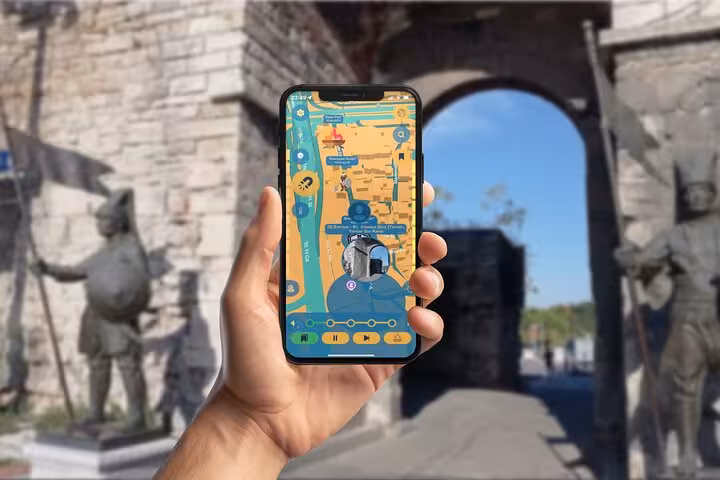 Hand holding smartphone with self-guided tour map app at Istanbul's historic Constantinople gate with medieval statues