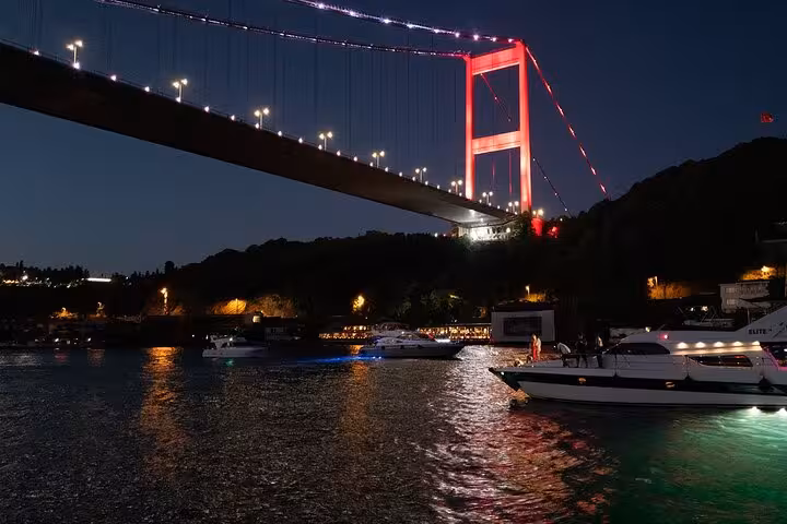 Bosphorus dinner cruise at night passing the illuminated Bosphorus Bridge in Istanbul with yachts on the water