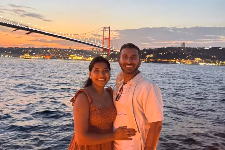Couple posing on luxury Bosphorus sunset cruise with illuminated 15 July Martyrs Bridge in Istanbul
