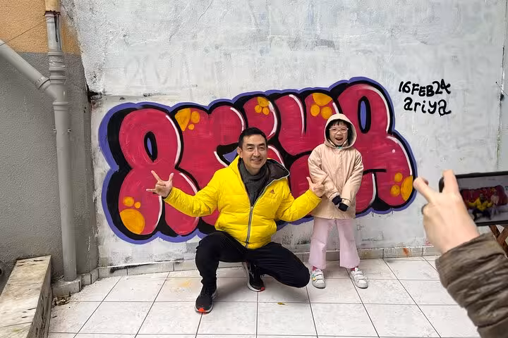 Guests posing by colorful graffiti mural during Istanbul Street Art Experience with local artists in home garden