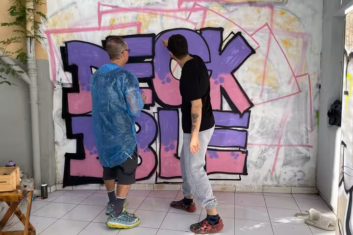 Local artists guide mural painting in Istanbul street art experience, outlining graffiti letters in a home garden