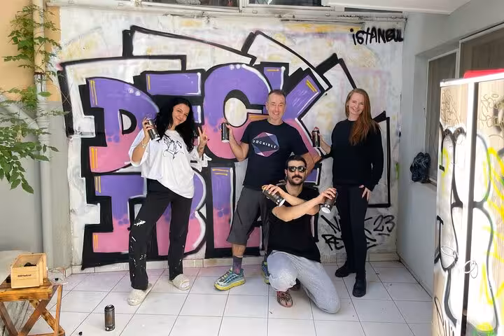 Travelers join Istanbul street art workshop, posing with spray cans by bold graffiti mural in a local studio