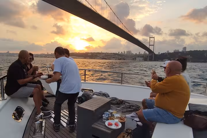 Guests enjoy snacks on a luxury yacht under the Bosphorus Bridge at sunset on an Istanbul cruise
