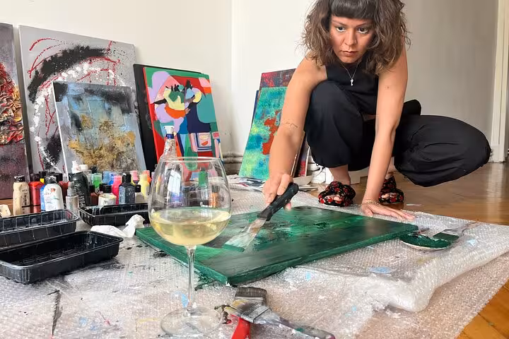 Artist paints green abstract canvas beside a glass of wine at Istanbul wine and paint workshop in a local home