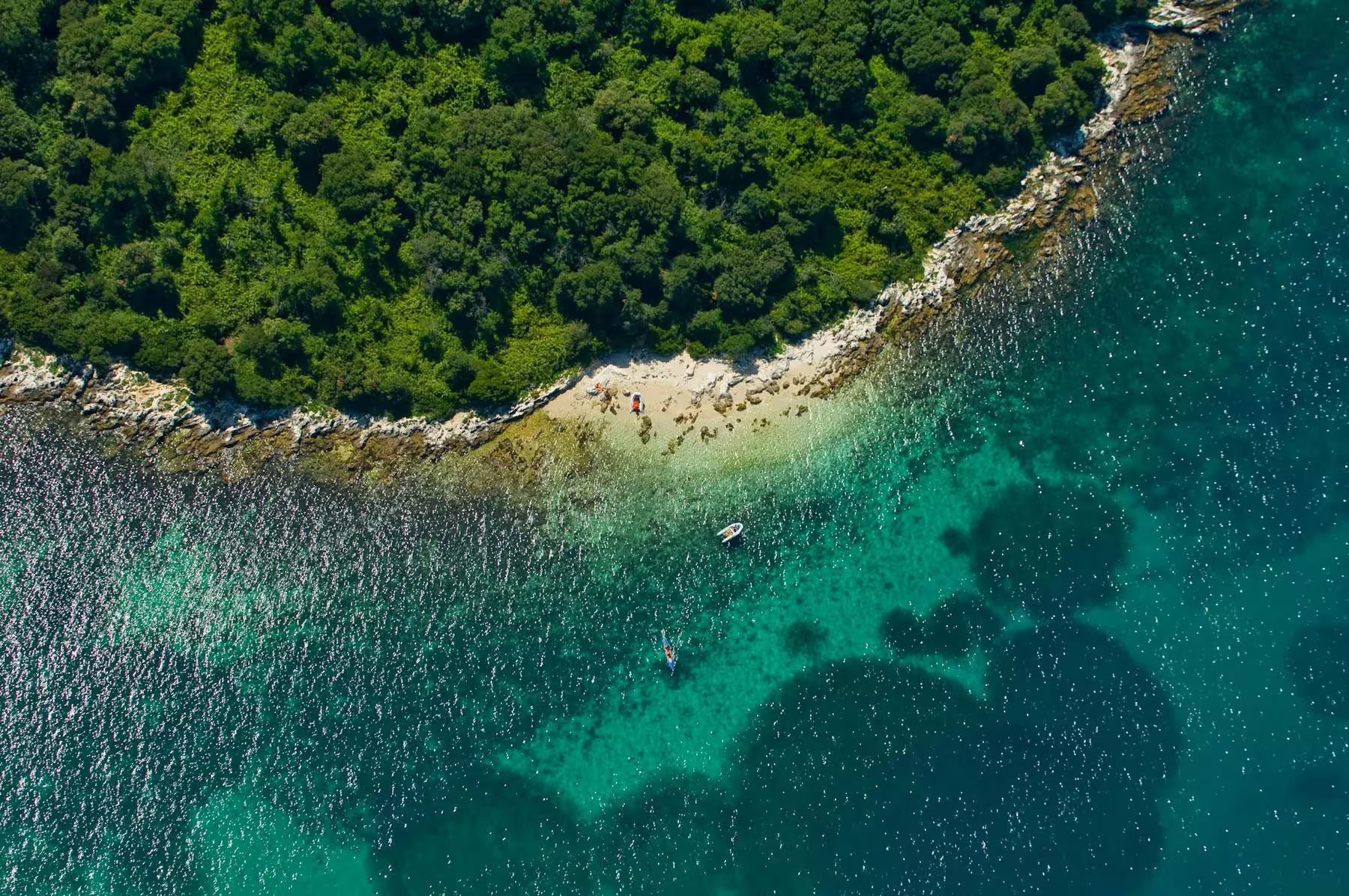 Aerial view of secluded Istrian cove with turquoise water and rocky shore, swimming stop on Poreč BBQ boat cruise