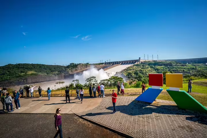 Visitors at Itaipu Dam viewing area, admiring the impressive hydroelectric facility with vibrant art installations nearby.