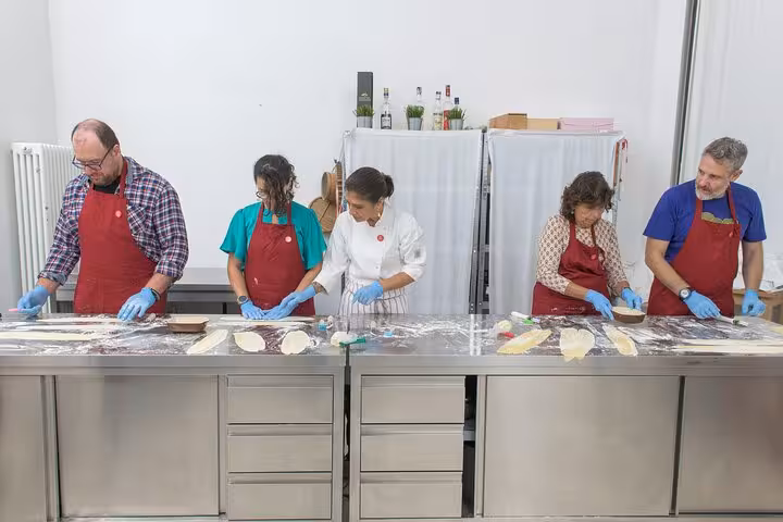 Participants in an Italian cooking class wearing aprons and gloves, learning to make pasta with an expert chef.