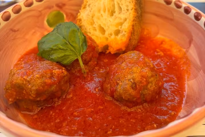 Close-up of Italian meatballs in rich tomato sauce with bread and basil, served at a Sorrento wine pairing lunch.