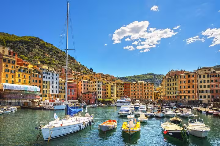 Colorful waterfront buildings and sailboats in a sunlit Italian Riviera harbor with turquoise water