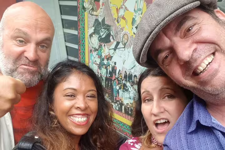 Four smiling friends posing for a selfie in front of a colorful London street mural