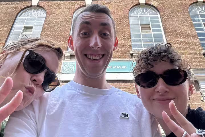 Three smiling friends posing for a selfie in front of a brick building during a London walking tour