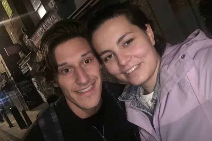 Two smiling visitors posing for a selfie on a London street at night during a Jack the Ripper walking tour
