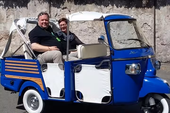 Tourists enjoying a James Bond-themed ride in a blue Ape Calessino on a sunny day.