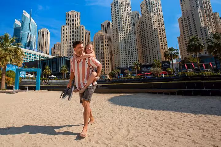 Father and daughter enjoying a playful moment on JBR Beach with Dubai Marina skyscrapers in the background.